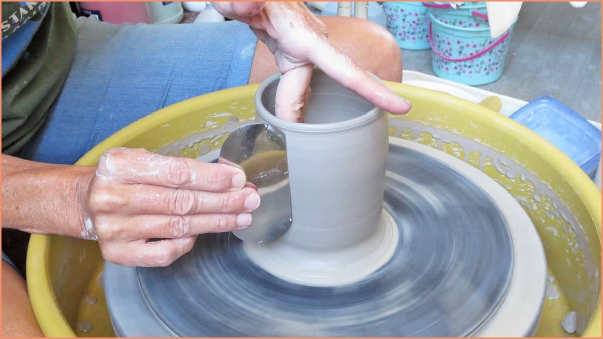 a picture of a potter using a metal scraper on the pottery wheel