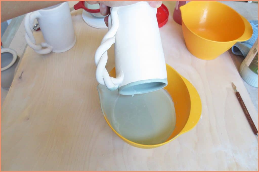 a picture of a potter glazing the inside of a mug