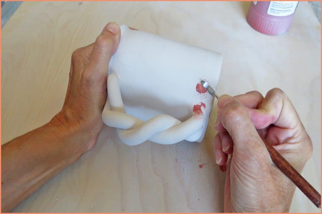 a picture of a potter removing glaze dripwith clean up tool