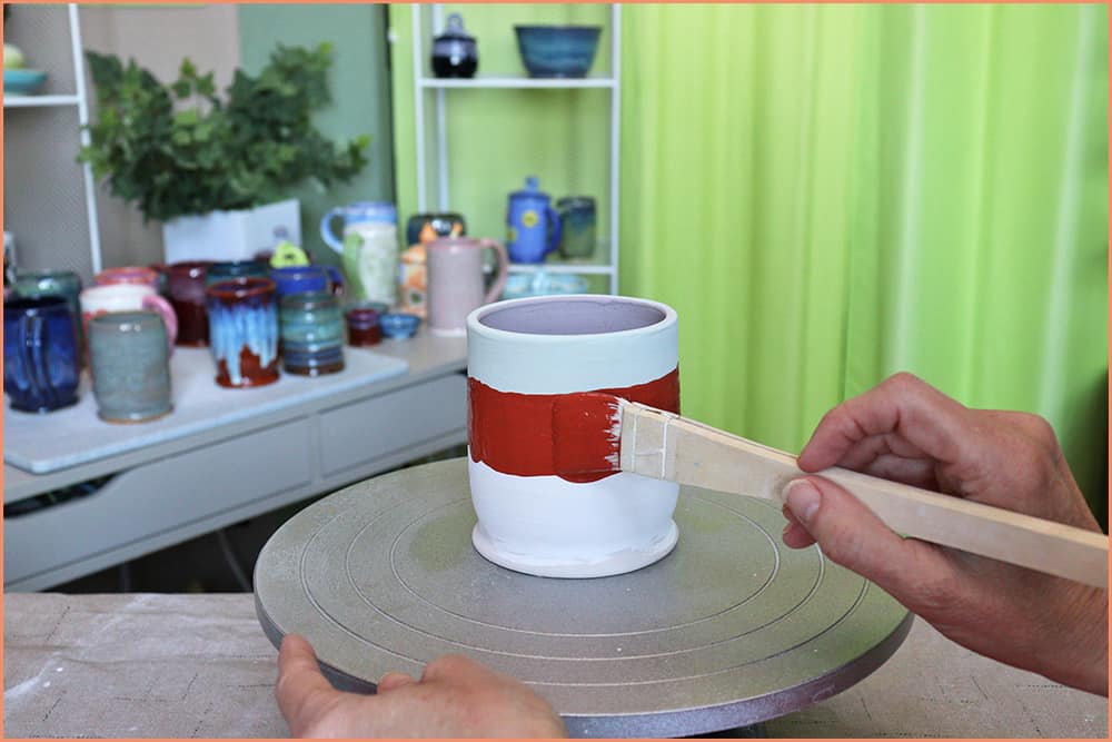 a picture of a potter brush glazing a merlot strip on a mug