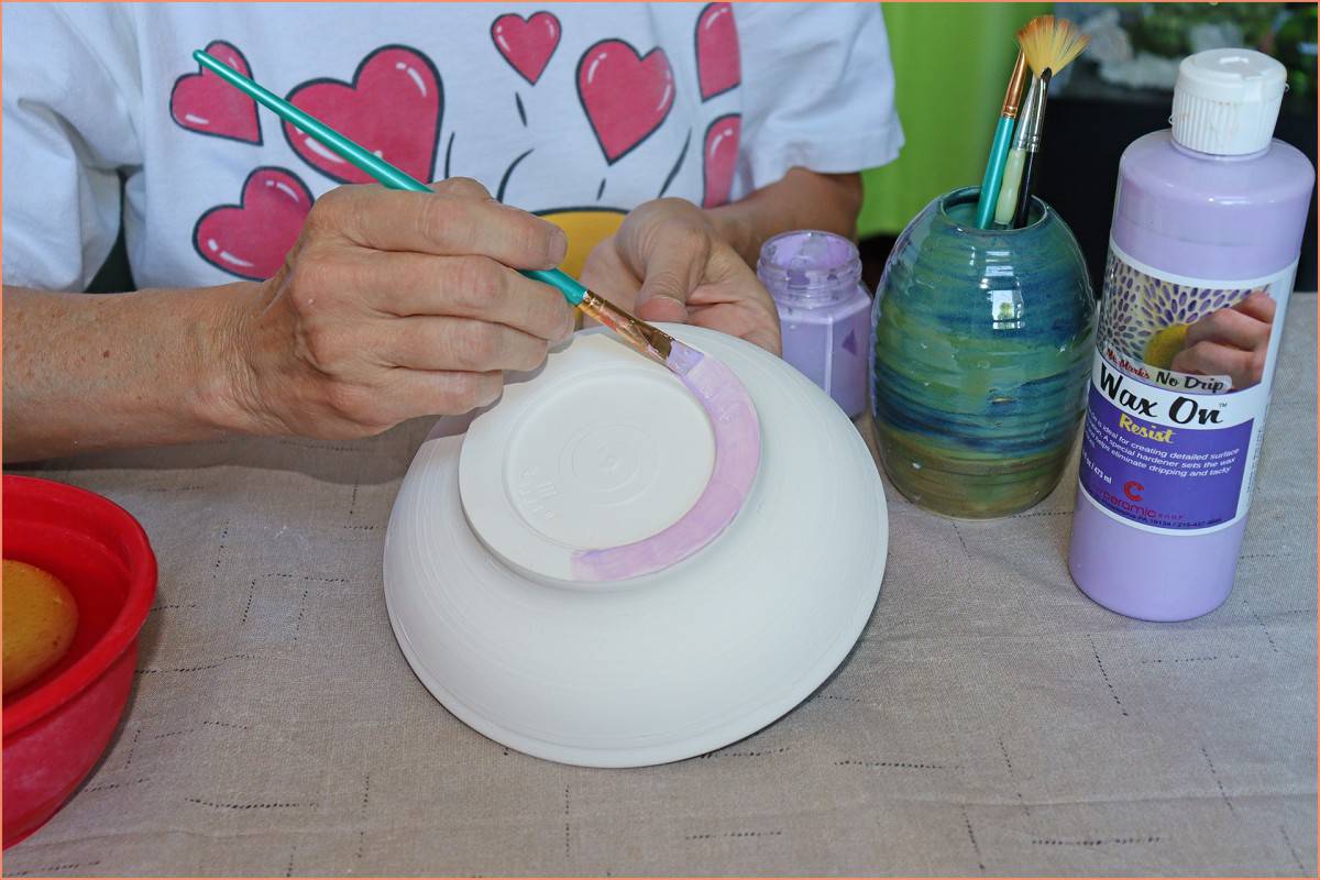 a picture of a potter applying wax resist with a sponge