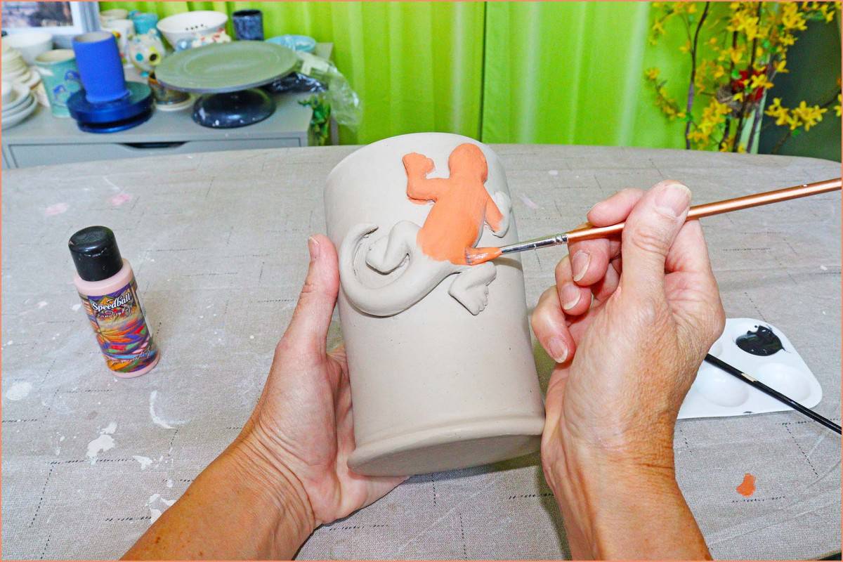a picture of a potter brushing on orange underglaze