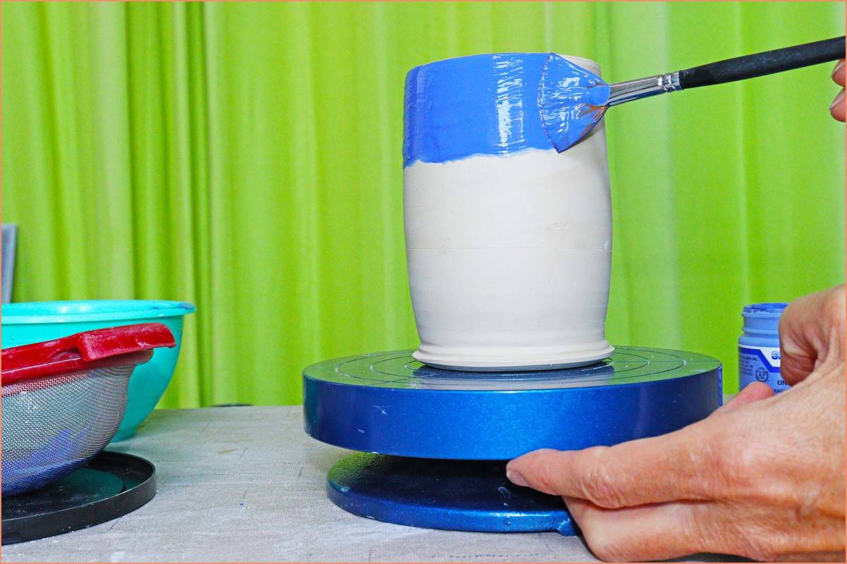 a picture of a potter brushing underglaze on a banding wheel