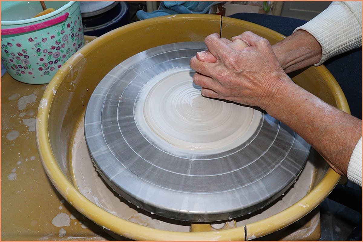 an image of a potter pressing clay out on the wheel