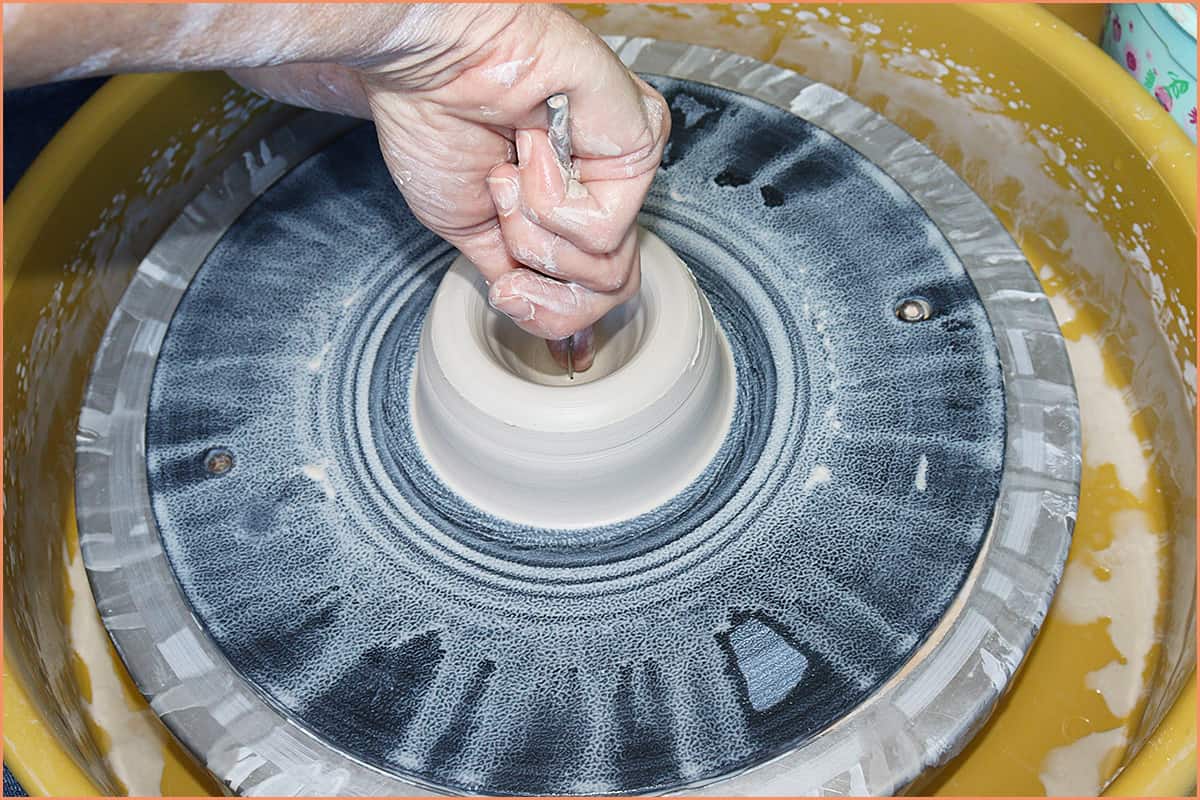 an image of a potter sliding finger down the needle tool
