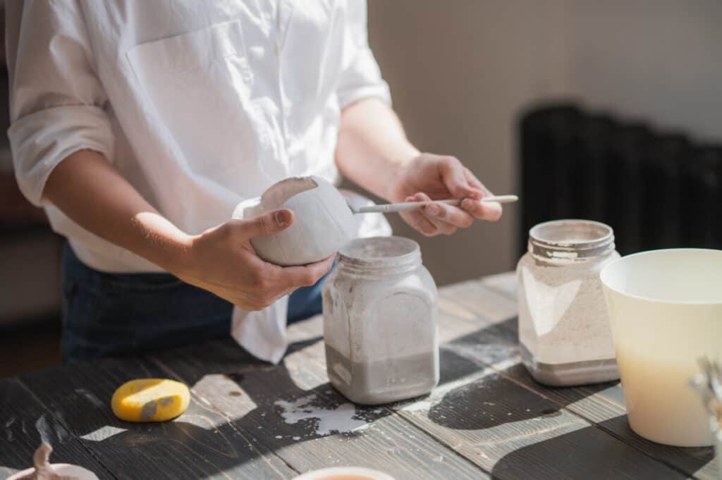 an image of potter glazing raw unburned ceramic cup using brush.